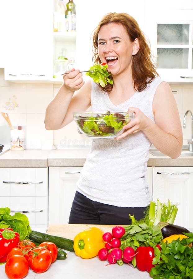 A Smiling Young Woman Eating Fresh Salad in Modern Kitchen Stock Image