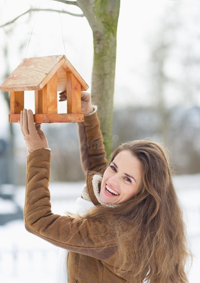 Smiling young woman hanging bird feeder on tree