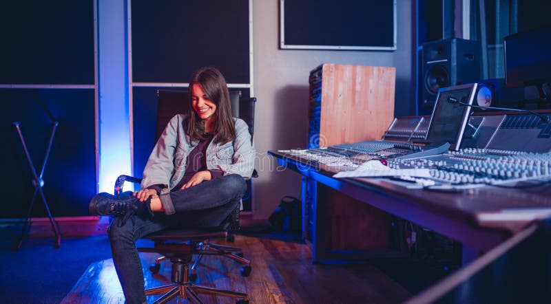 Smiling young woman sitting at music mixing desk. happy female sound engineer at sound recording studio. Smiling young woman sitting at music mixing desk. happy female sound engineer at sound recording studio.