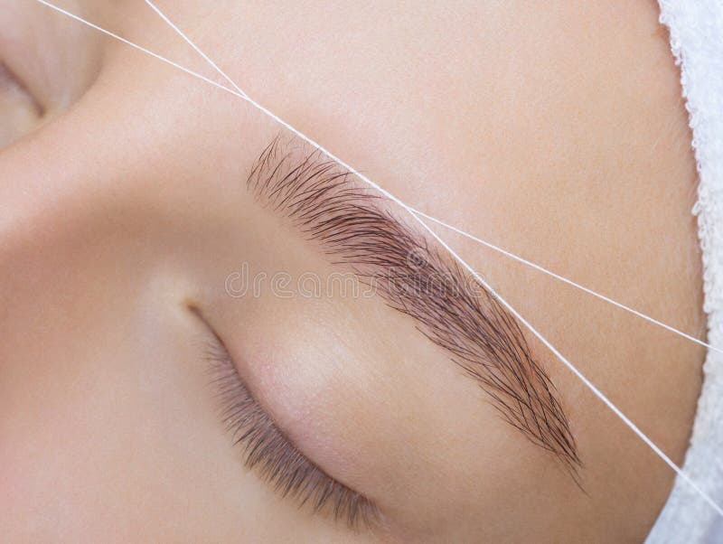 The make-up artist plucks her eyebrows with a thread close-up. Face care beauty treatments in the beauty salon. The make-up artist plucks her eyebrows with a thread close-up. Face care beauty treatments in the beauty salon.