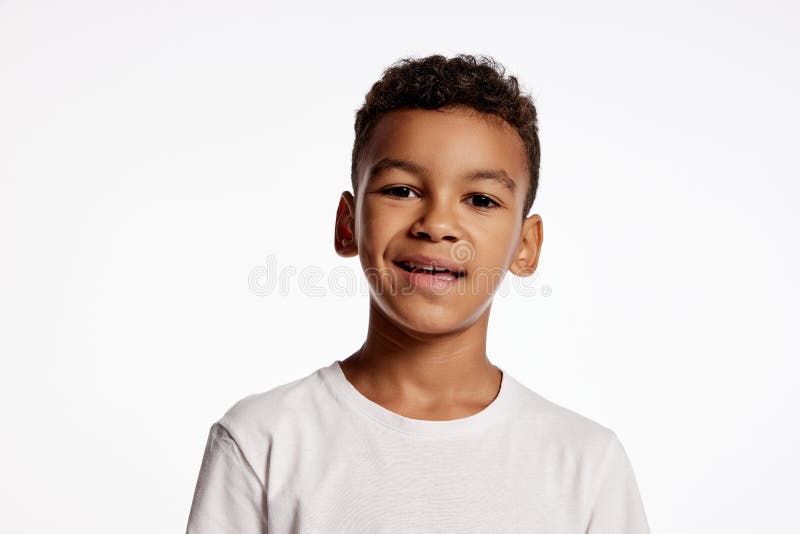 Smirk. Half-length portrait of african little boy in white tee expressing emotions isolated over white background. Kids