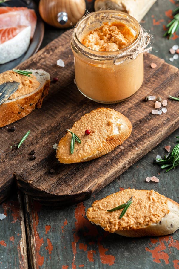 Smoked salmon and soft cheese spread, mousse, pate in a jar with sliced bread on a wooden background. vertical image, place for
