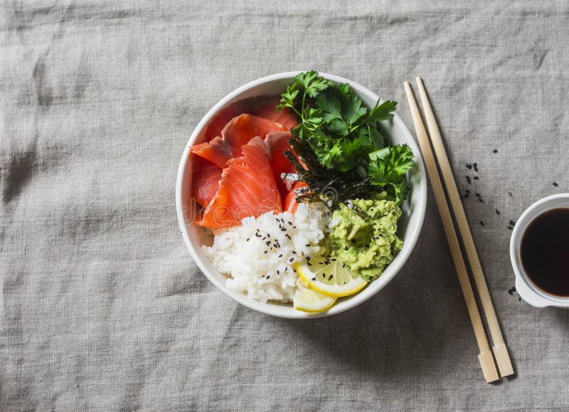 Smoked salmon sushi bowl on grey background, top view. Rice, avocado puree, salmon - healthy food concept. Asian style