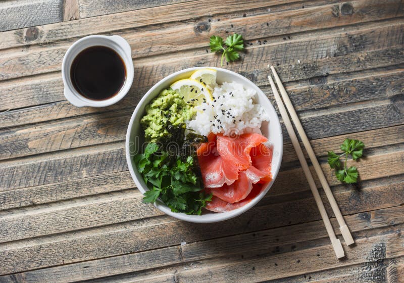Smoked salmon sushi bowl on wooden background, top view. Rice, avocado puree, salmon - healthy food