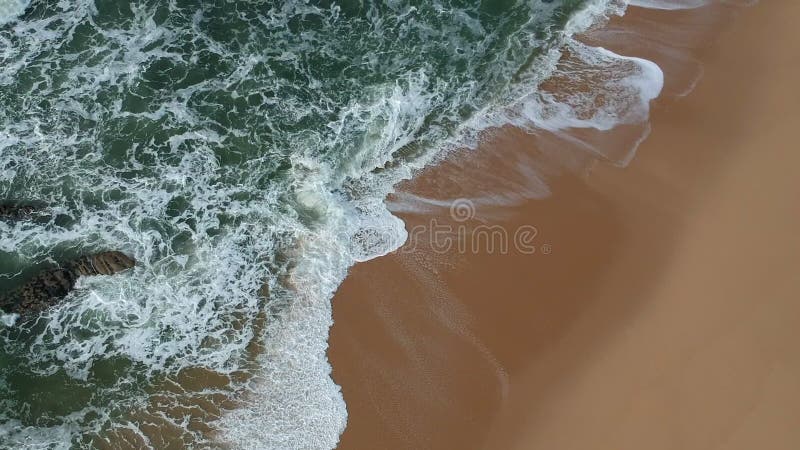 Smooth moving aerial shot of blue ocean waves crashing on golden sandy beach in Portugal