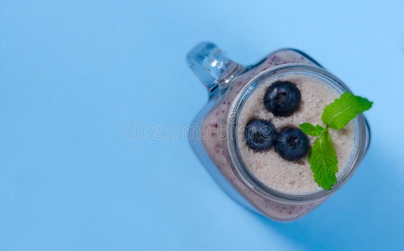 Smoothie голубики с мятой в glas опарника каменщика с ягодами и мятой Над взглядом на голубой таблице стоковые изображения Smoothie голубики с мятой в glas опарника каменщика с ягодами и мятой Над взглядом на голубой таблице стоковые изображения