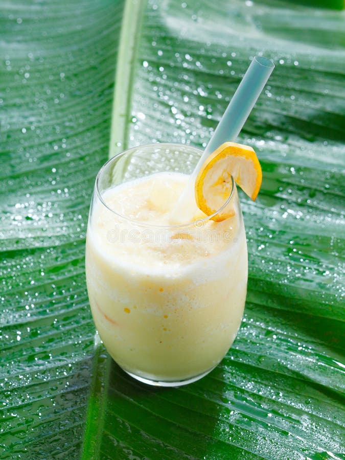 High angle view of a single glass of chilled banana smoothie or blended cocktail served on a banana frond with copyspace. High angle view of a single glass of chilled banana smoothie or blended cocktail served on a banana frond with copyspace