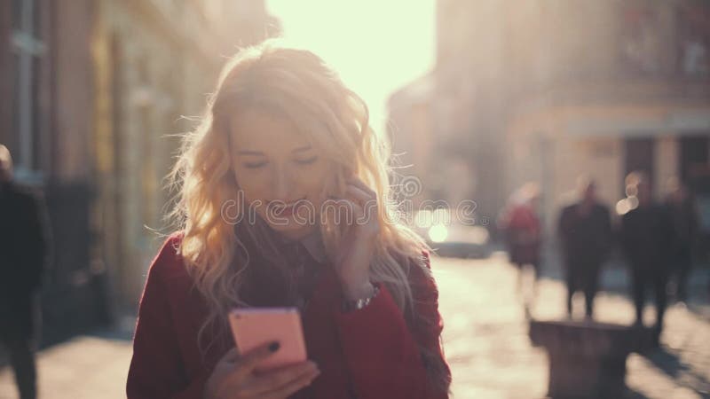 Sms da mulher de negócio que texting usando o app no telefone esperto Menina atrativa no revestimento vermelho que anda na cidade