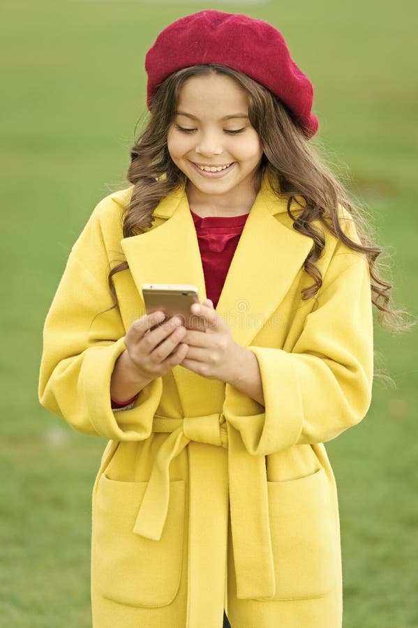 Sms to friend. small child write sms on phone. beauty in autumn coat. cheerful little girl in yellow coat. parisian girl royalty free stock images