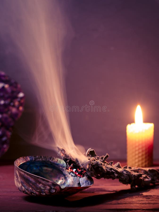 Smudging sage with dense smoke. Copy space. Amethyst crystal and burning bees wax candle at background. Smudging sage, amethyst an