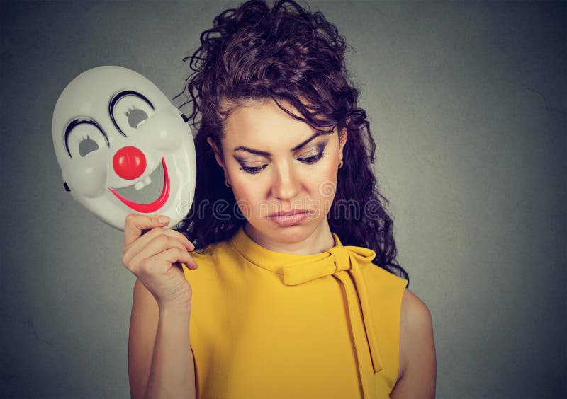 Portrait sad woman taking off clown mask expressing cheerfulness happiness on gray wall background. Portrait sad woman taking off clown mask expressing cheerfulness happiness on gray wall background