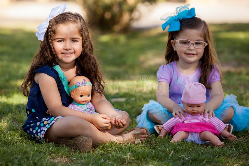 Portrait of a couple of beautiful girls playing with their dolls at a park. Portrait of a couple of beautiful girls playing with their dolls at a park