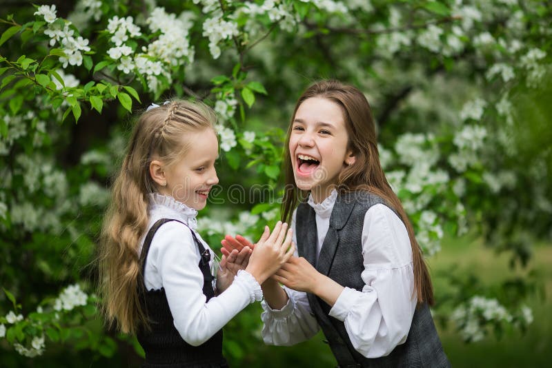 Funny girls in stylish school uniforms play outdoors in the blossoming apple park. Funny girls in stylish school uniforms play outdoors in the blossoming apple park