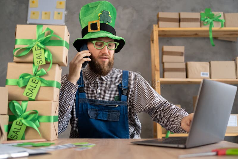 Småföretagsägare startar och bedriver handel. man i leprechaun som hanterar onlinebutikens affärsman som svarar på telefonsamtal arkivbild