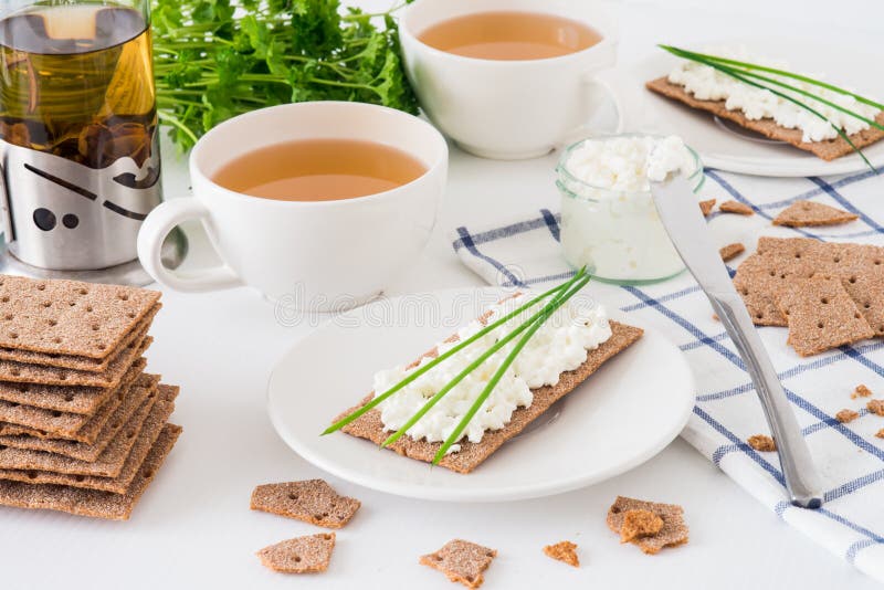 Snack with fresh tea and rye crispy bread Swedish crackers with cottage cheese, decorated with thin green onion, on white backgr