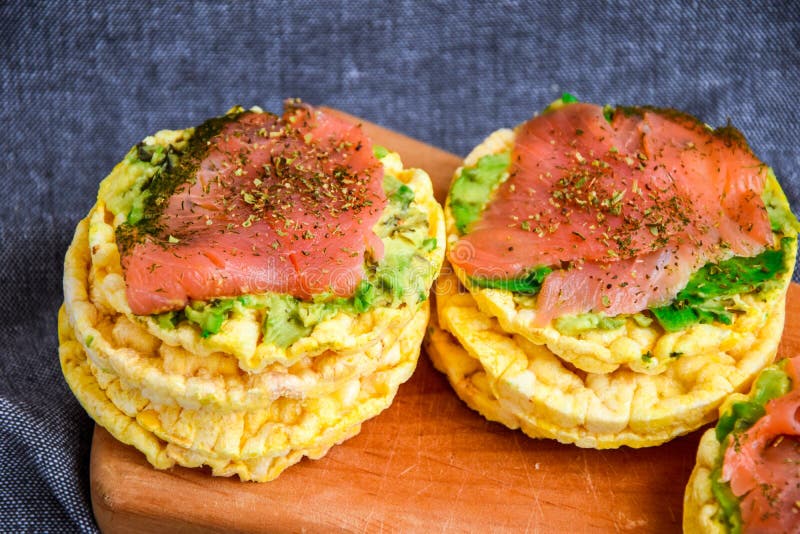 Snacks from rice cakes, salmon, avocado and spices on cutting board , gluten free bread, guacamole