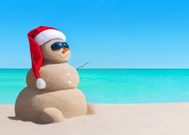 Sneeuwman in de hoed van de Kerstmiskerstman en zonnebril op zee strand