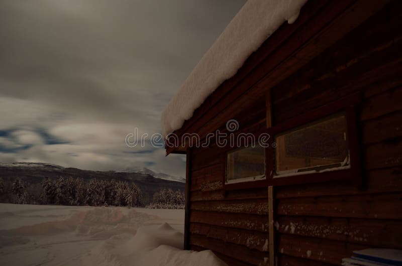 Snow covered garage in winter with mountain and field background at night. Arctic, outside.