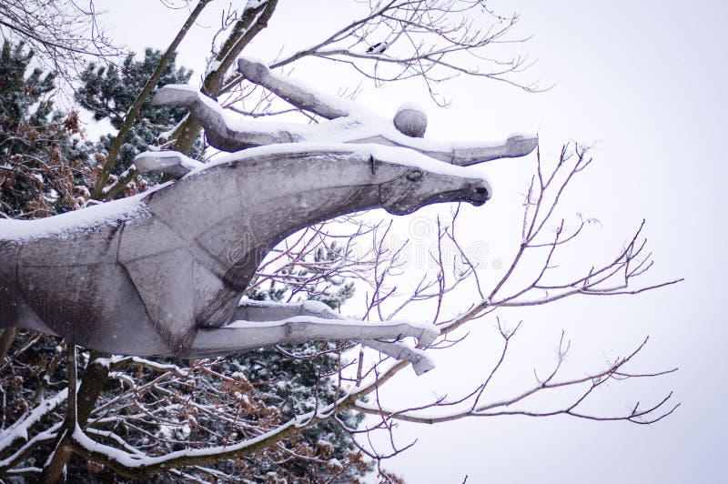 Snow covered horse statue flying with his rider, trees background