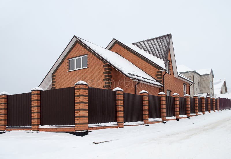 Snow covered red brick house with metal fence