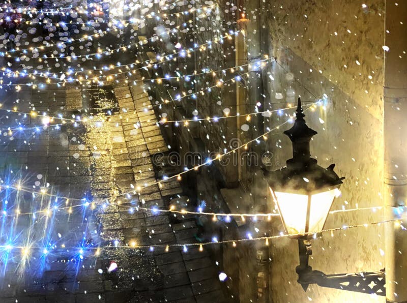 View from window glass on evening Christmas street , yellow lantern lamp illumination and light blurred on wet pavement in medieva