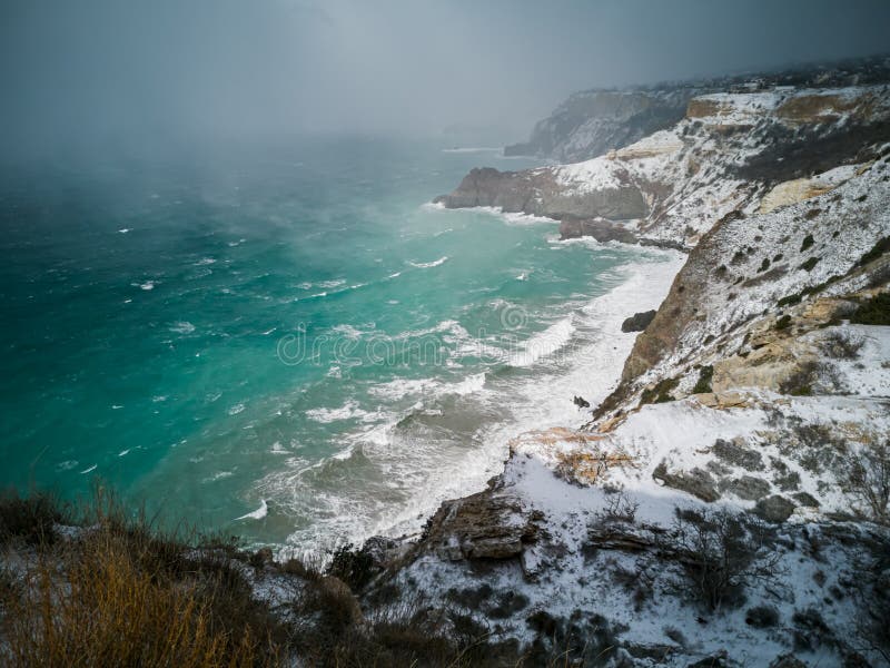 A snow storm covered the seashore. Bright turquoise sea, squally wind, huge waves, bright sun