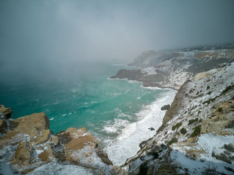 A snow storm covered the seashore. Bright turquoise sea, squally wind, huge waves, bright sun