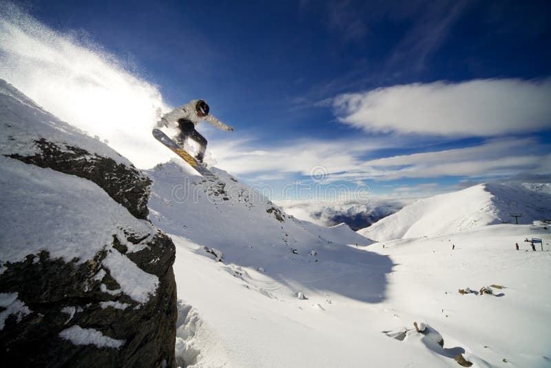 Snowboarder a cavallo scogliera con profondo cielo blu sullo sfondo.