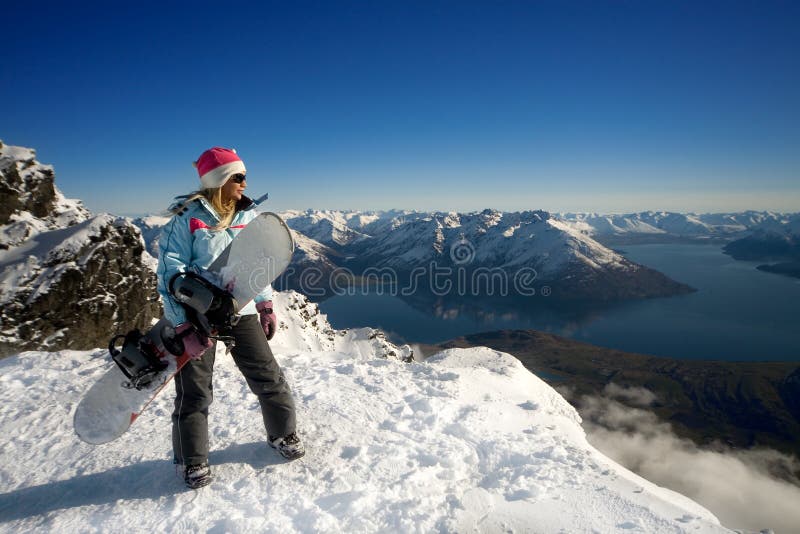 Žena s snowboard, ktorý stojí na vrchole zasnežené hory.