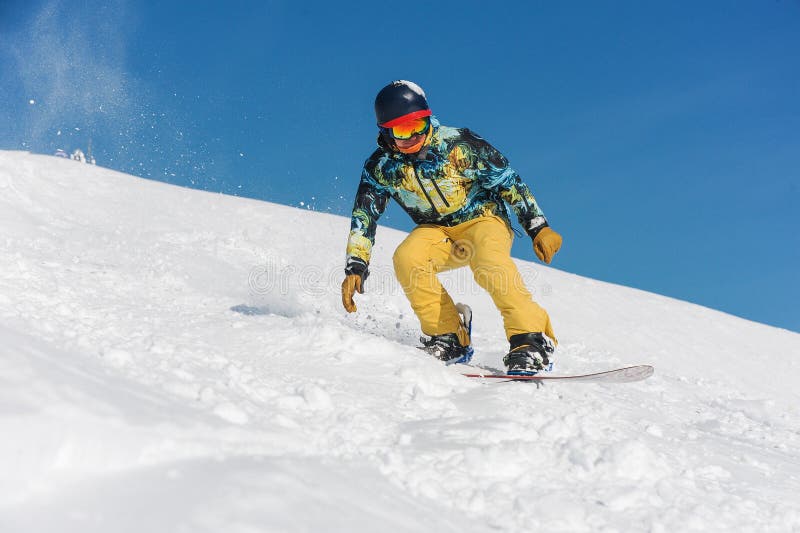 Snowboarder in abiti sportivi luminosi che guidano giù un pendio di montagna fotografie stock libere da diritti Snowboarder in abiti sportivi luminosi che guidano giù un pendio di montagna fotografie stock libere da diritti