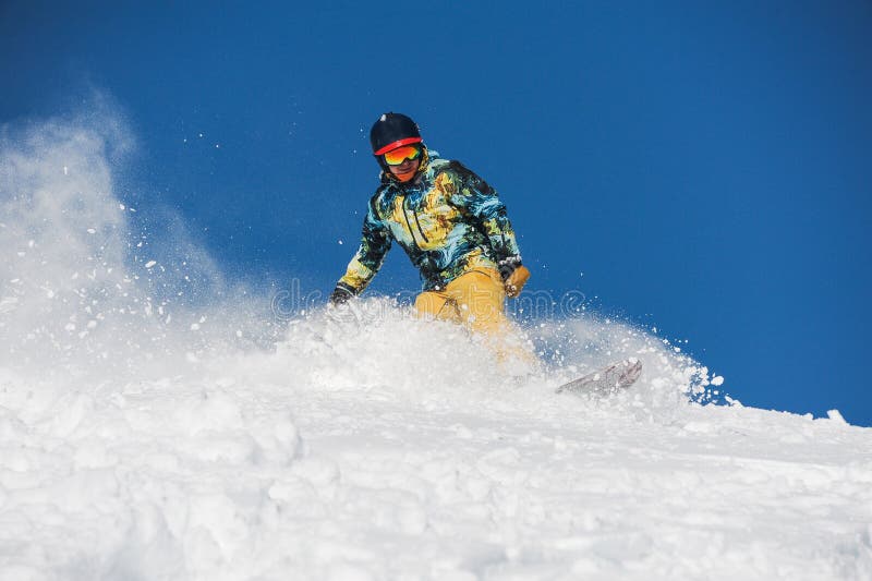 Snowboarder in abiti sportivi luminosi che guidano giù un pendio di montagna della polvere immagini stock libere da diritti Snowboarder in abiti sportivi luminosi che guidano giù un pendio di montagna della polvere immagini stock libere da diritti