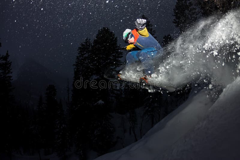 Snowboarder parasitario que salta en la noche con un trampolín en el bosque fotografía de archivo libre de regalías Snowboarder parasitario que salta en la noche con un trampolín en el bosque fotografía de archivo libre de regalías