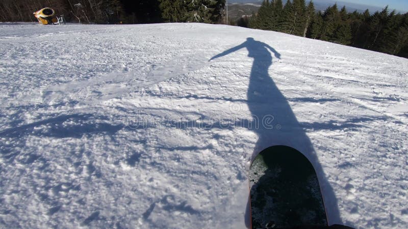 Snowboarderverschiebung auf einem Snowboard, den sein Schatten vor ihm auf dem Schnee synchron bewegt sich