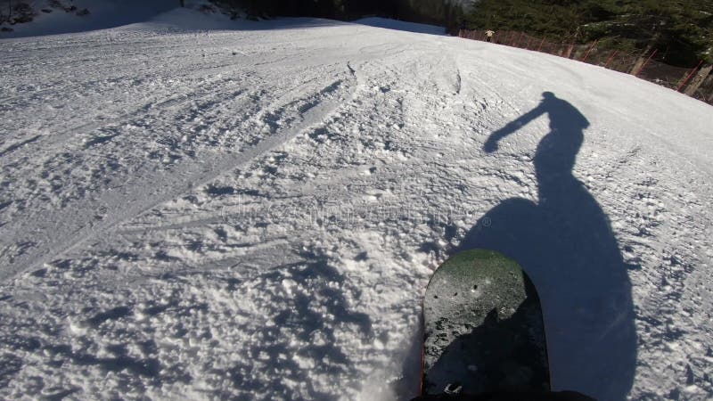 Snowboarderverschiebung auf einem Snowboard, den sein Schatten vor ihm auf dem Schnee synchron bewegt sich