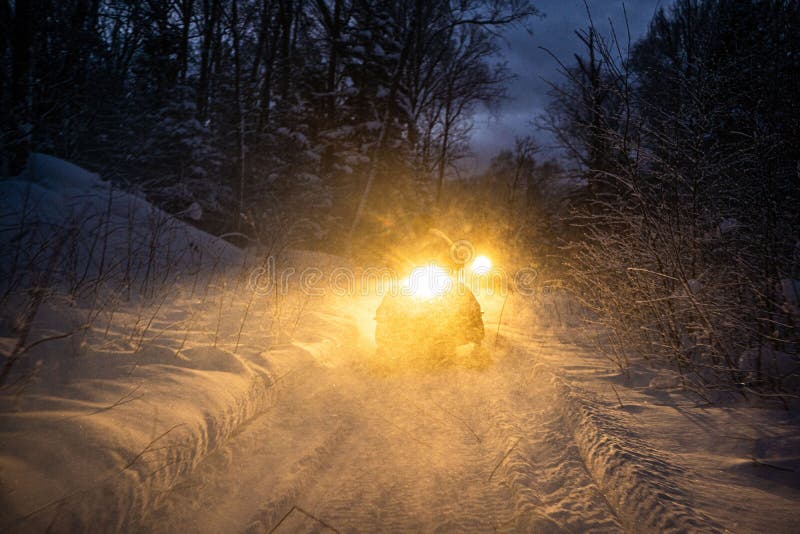 Snowmobile in the evening goes through the winter forest. headlights. night road through the winter forest. snowmobile