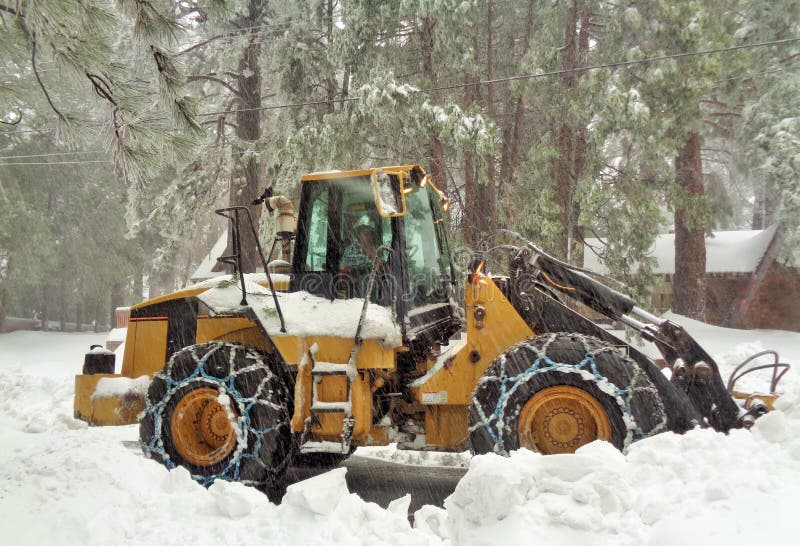 This is an image of a giant tractor snowplow clearing snow from a residential road in a mountain snow storm. Pine trees in the background are quickly being covered in the falling snow. It is a freezing winter day as the snowplow driver goes about doing his job. In the foreground there is a large berm created from the snow, that has been scraped up from the road. It is deposited at the sides of the roads as the plow moves down the street. It could be used to represent the cold winter season, removing barriers, hard working people, people we depend on, public services, safety, strength. This is an image of a giant tractor snowplow clearing snow from a residential road in a mountain snow storm. Pine trees in the background are quickly being covered in the falling snow. It is a freezing winter day as the snowplow driver goes about doing his job. In the foreground there is a large berm created from the snow, that has been scraped up from the road. It is deposited at the sides of the roads as the plow moves down the street. It could be used to represent the cold winter season, removing barriers, hard working people, people we depend on, public services, safety, strength.