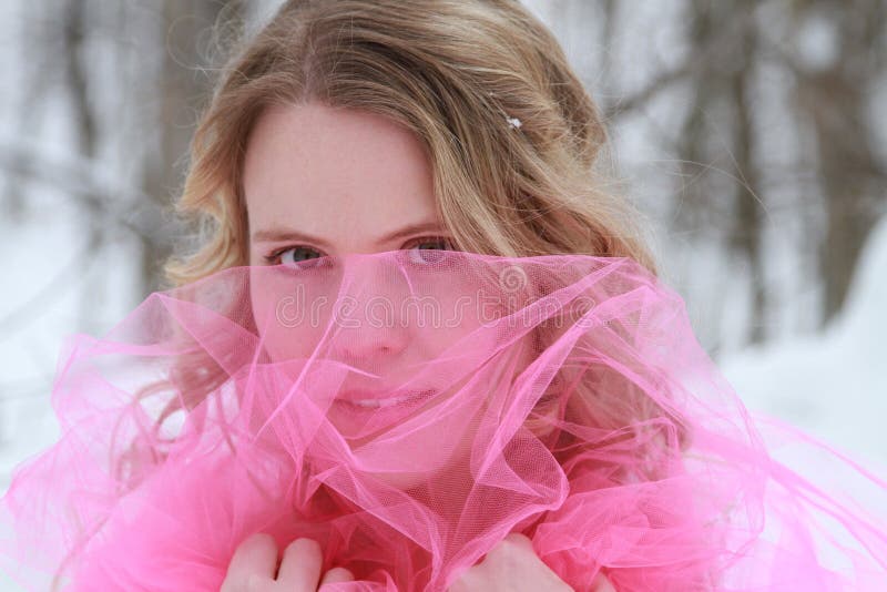 An beautiful young woman peering through bright pink tulle in a snowy forest. An beautiful young woman peering through bright pink tulle in a snowy forest.