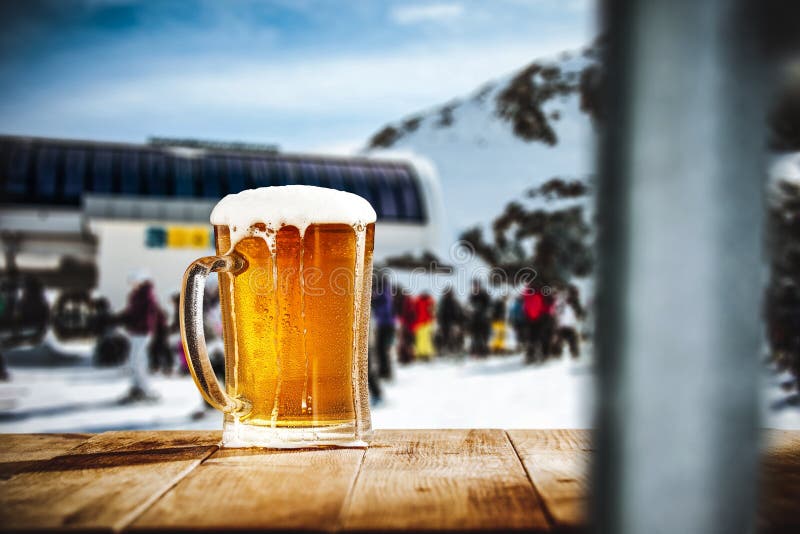 Glass of beer on wooden table. Blurred snowy white winter sunshine landscape with table top for products and decorations.