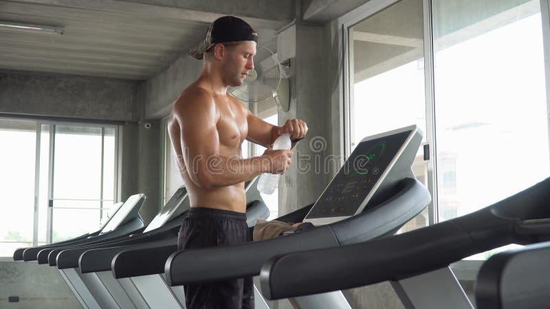 Snygg muskelman som kör på träskkvarn har sytt dricksvatten och torkat svett med handduk i gym för fitness. skjortlös stock video