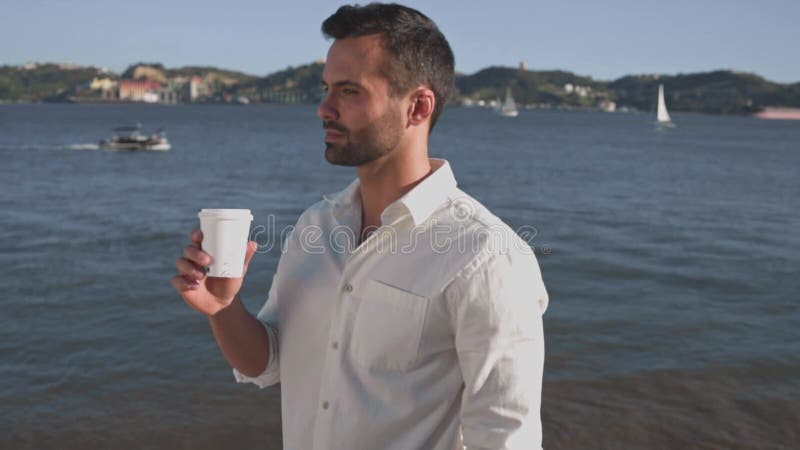 Snygg pojke vid floden och leende kaffe. lager videofilmer