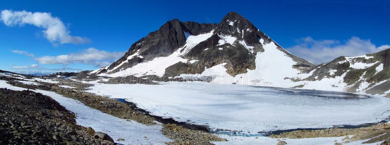 Beautiful scenery, the view of a landscape of snow summit, rocky mountain peaks and glacier in Norway. Lake covered with snow and ice, iceberg, deep blue clear water, sunny day, blue sky with some clouds. Norwegian mountains of Jotunheim national park. Beautiful scenery, the view of a landscape of snow summit, rocky mountain peaks and glacier in Norway. Lake covered with snow and ice, iceberg, deep blue clear water, sunny day, blue sky with some clouds. Norwegian mountains of Jotunheim national park.