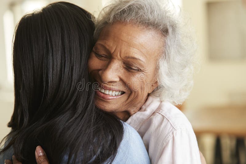 Sobre a opinião do ombro a mãe superior que está sendo abraçada pela filha adulta em casa fotografia de stock Sobre a opinião do ombro a mãe superior que está sendo abraçada pela filha adulta em casa fotografia de stock