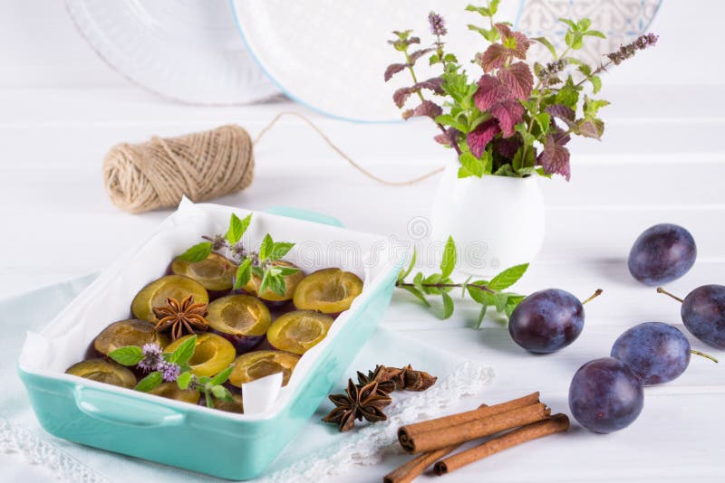 Sobremesa caseiro saudável Ameixas vermelhas cortadas prontas para cozinhar em um prato do cozimento com hortelã fresca, canela, imagem de stock Sobremesa caseiro saudável Ameixas vermelhas cortadas prontas para cozinhar em um prato do cozimento com hortelã fresca, canela, imagem de stock