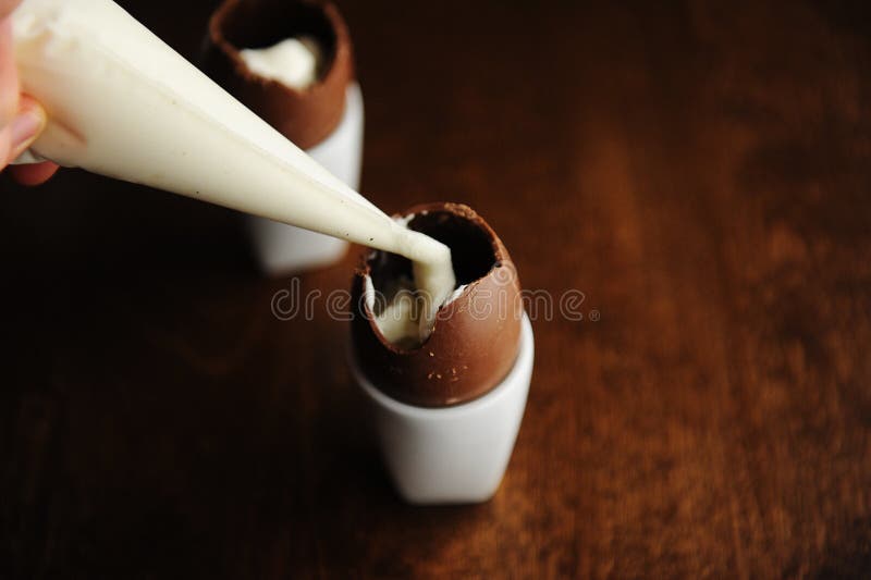 Sobremesa da Páscoa, processo de cozimento Expelindo o enchimento do saco da pastelaria no ovo de chocolate aberto Fundo escuro c imagem de stock royalty free Sobremesa da Páscoa, processo de cozimento Expelindo o enchimento do saco da pastelaria no ovo de chocolate aberto Fundo escuro c imagem de stock royalty free