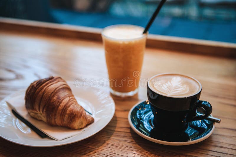 Sobremesa tradicional francesa do croissant ao lado do cappuccino e do suco de laranja do café em um café para o café da manhã foto de stock royalty free Sobremesa tradicional francesa do croissant ao lado do cappuccino e do suco de laranja do café em um café para o café da manhã foto de stock royalty free