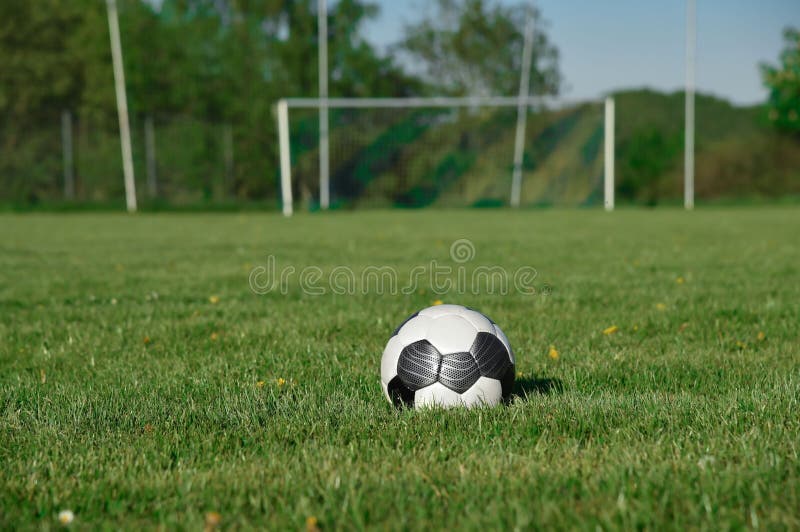 Soccer Ball Resting in an Empty Grassy Field in Front of a Goal Net