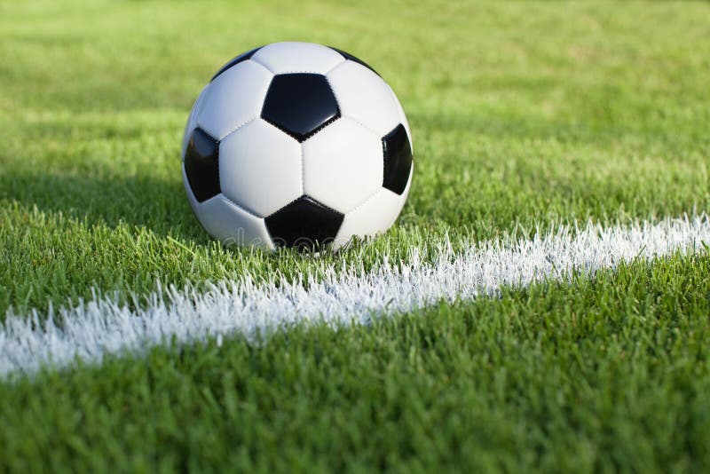 A traditional soccer ball sits on a grass field with white stripe. A traditional soccer ball sits on a grass field with white stripe