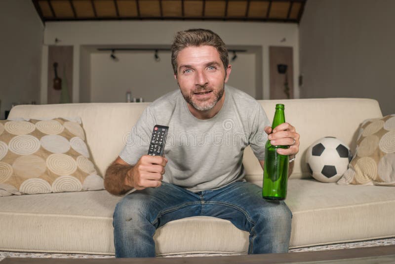Soccer supporter man enjoying game on television - happy and attractive football fan watching tv game at home sofa couch excited