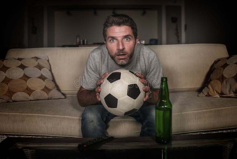 Soccer supporter man enjoying game on television - nervous and attractive football fan watching tv game at home sofa couch excited