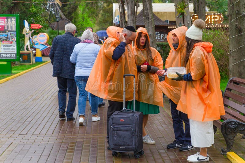 SOCHI, ROSJA, 21 2019 KWIECIEŃ - grupa turyści w Riviera parku ubierał w pomarańczowych deszczowach w chmurnej pogodzie obrazy stock SOCHI, ROSJA, 21 2019 KWIECIEŃ - grupa turyści w Riviera parku ubierał w pomarańczowych deszczowach w chmurnej pogodzie obrazy stock